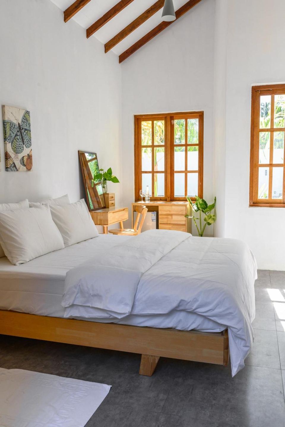 A bright Kondey Villas guest room with a white double bed, timber furniture and windows onto palms